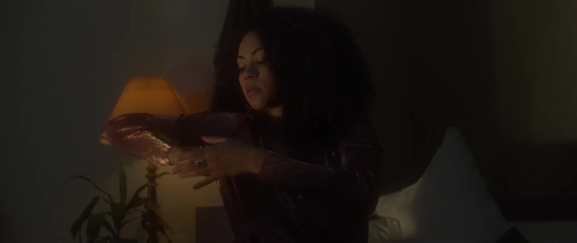 A woman sits on a bed gyrating in a dark room