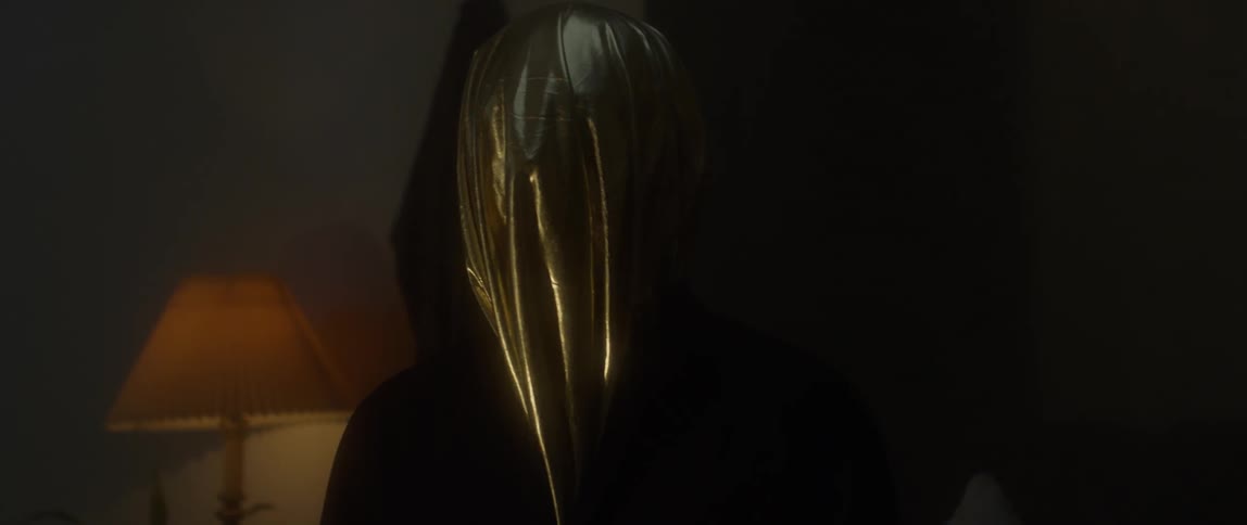 Lights cast shadows on the covered head of a person sitting in a room