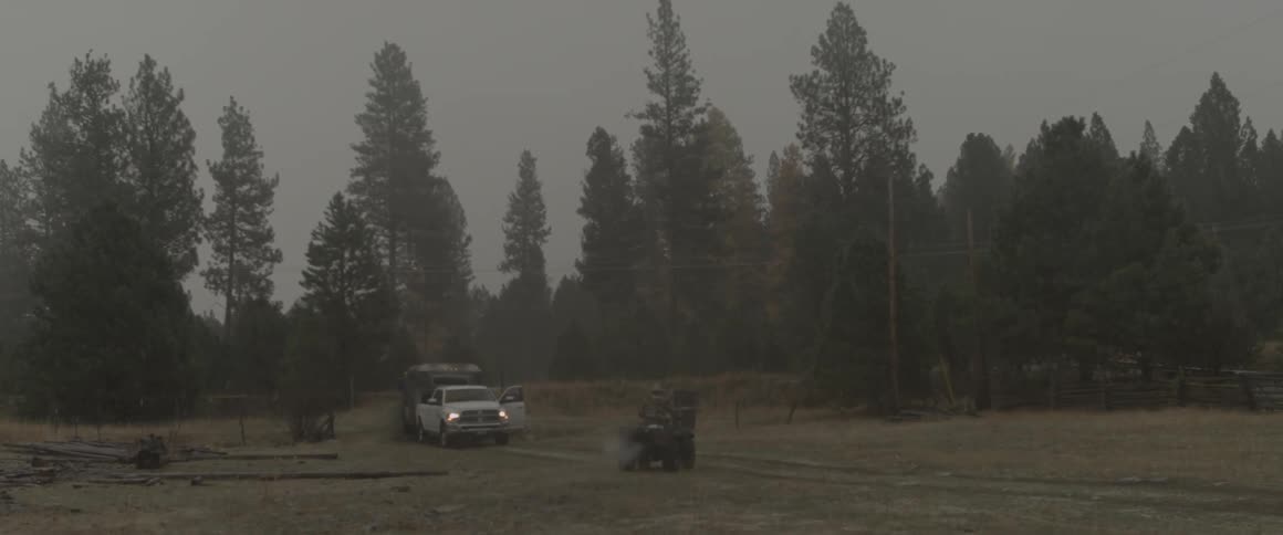 A man on an atv rides through a field toward a pickup truck