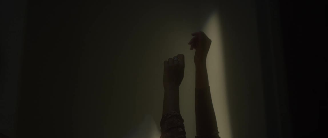 A woman stretches her arms into the air while laying in a dark room
