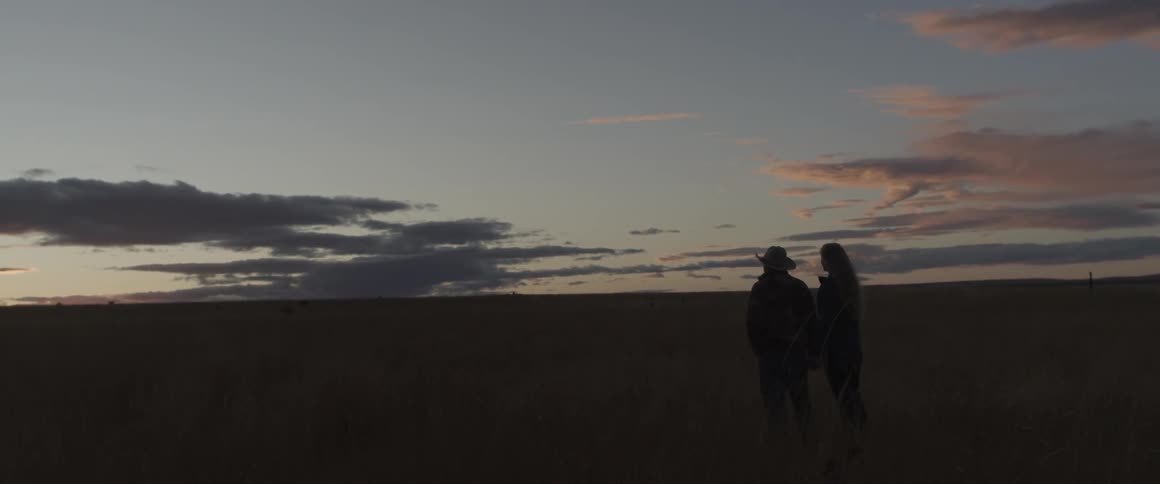 Man and woman stand in a large field at sunset