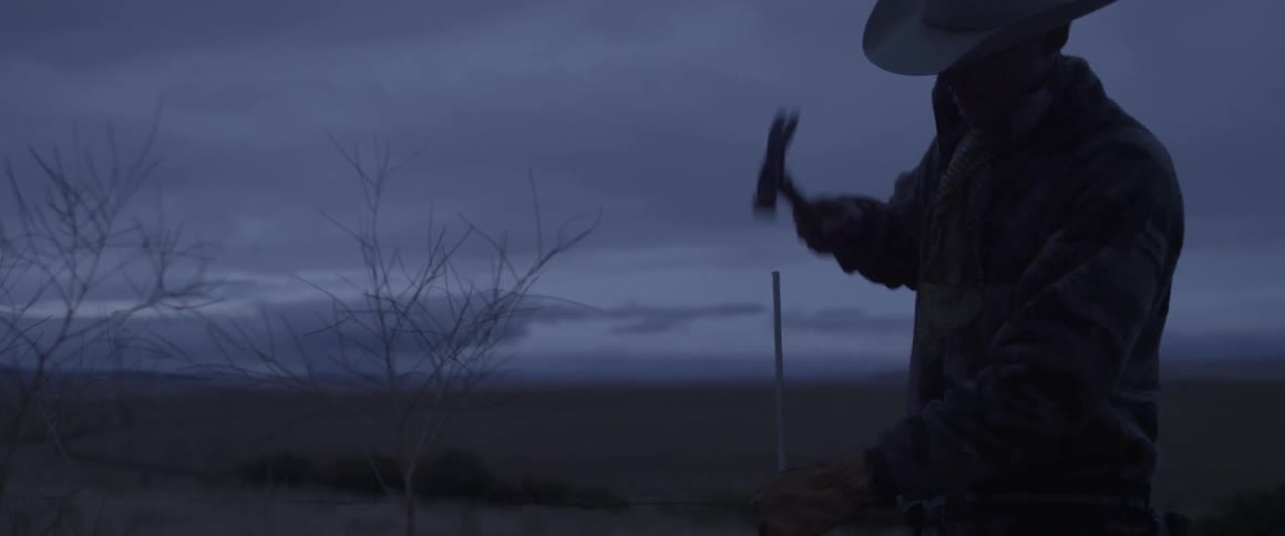 A man is repairing a fence on a ranch at dusk