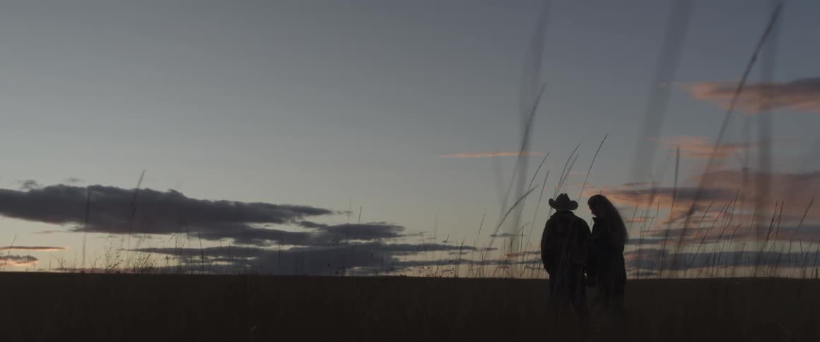 Man and woman hold hands while standing in a field