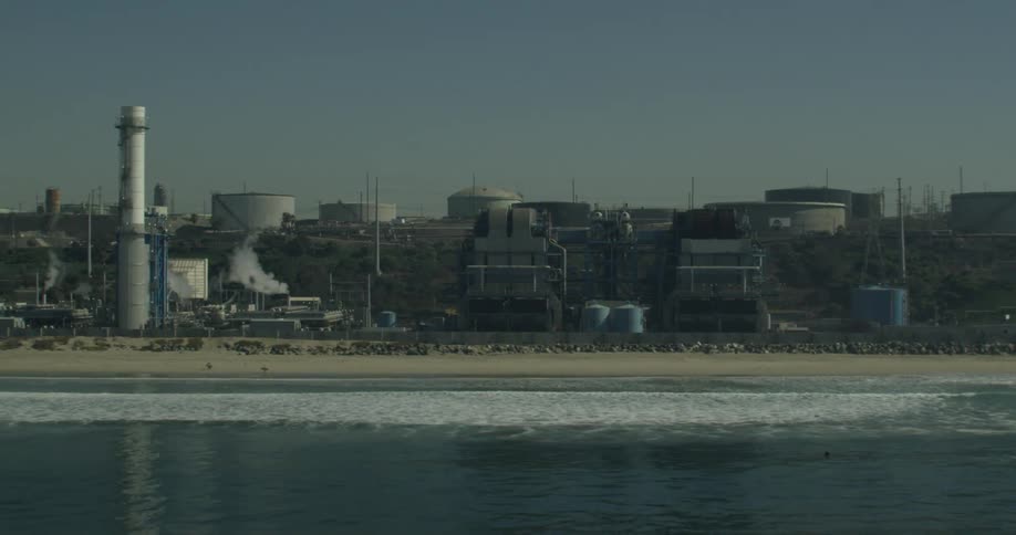 Waves splashing to a sandy shore next to the industrial part of a city in California