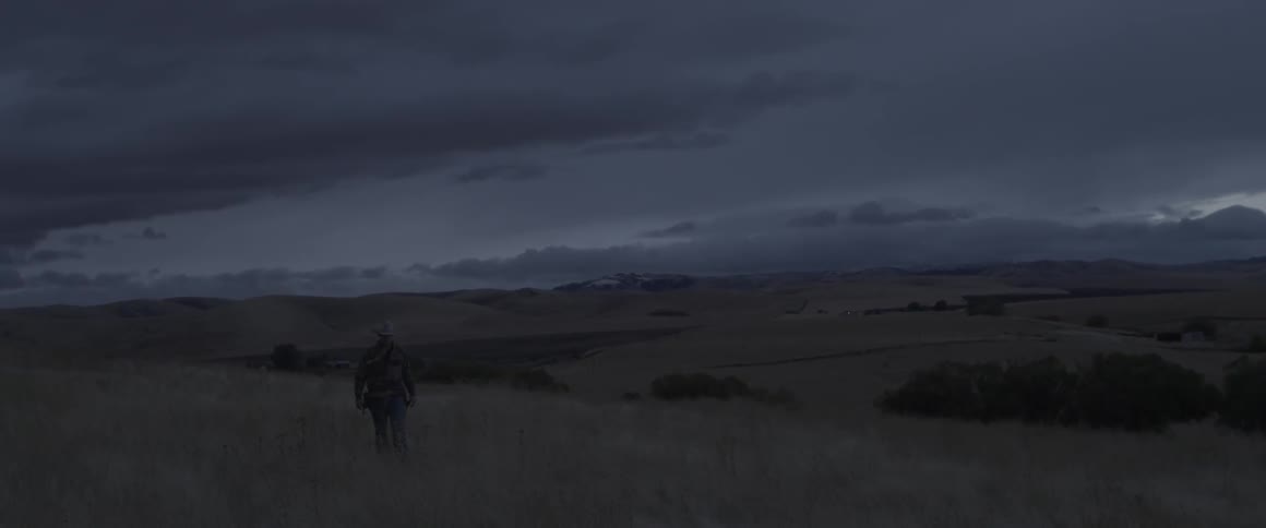 A rancher walks on a grassy hillside at dusk