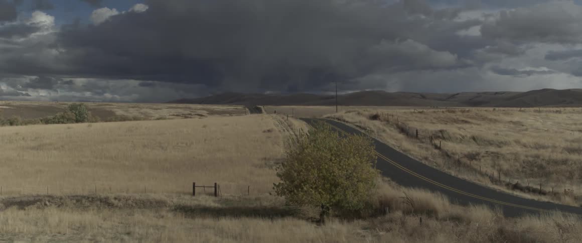 Storm clouds drop rain on the horizon beyond a rural road