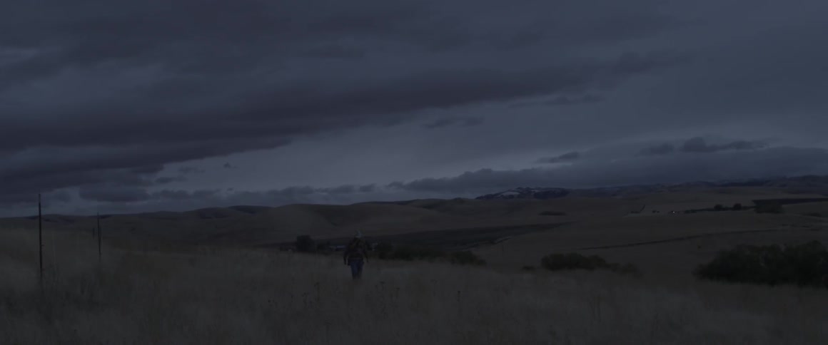 A man walks across the grass at sunset