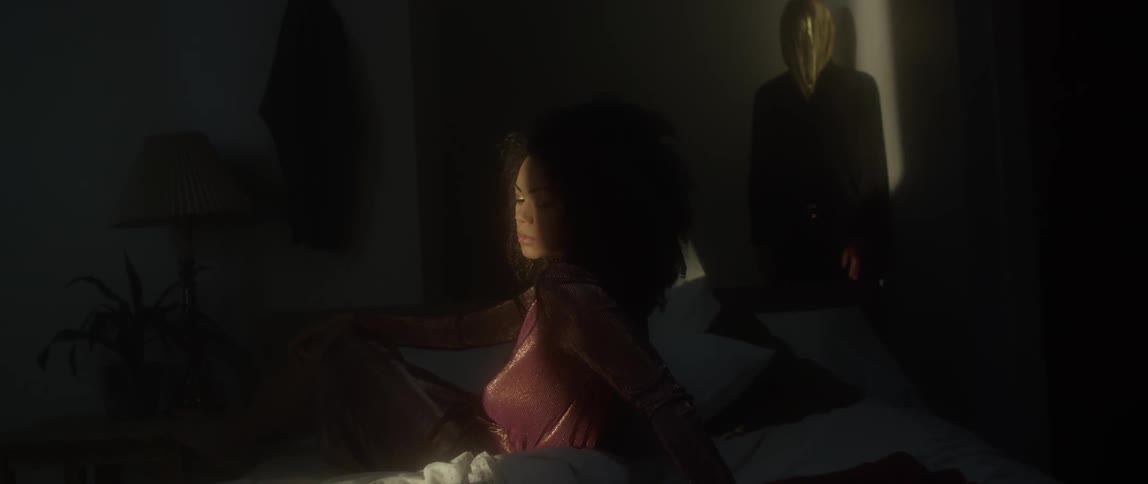 This woman sits in a dark room with a person behind her