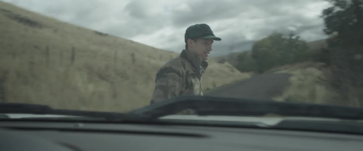 A man wearing camo walks around a car on a road
