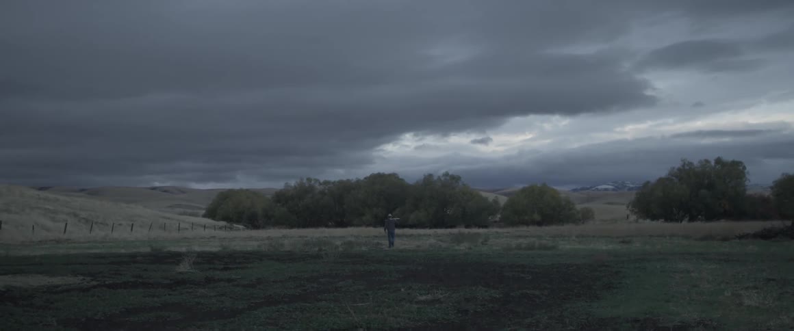 A man is walking across the long field on a stormy day