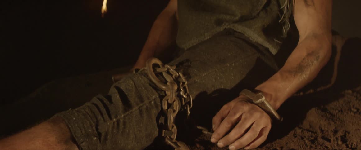 A violin is on the ground near a chained man