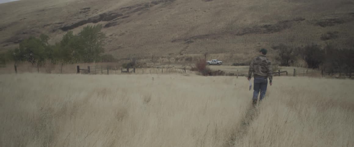 A man walks in an open field towards a truck