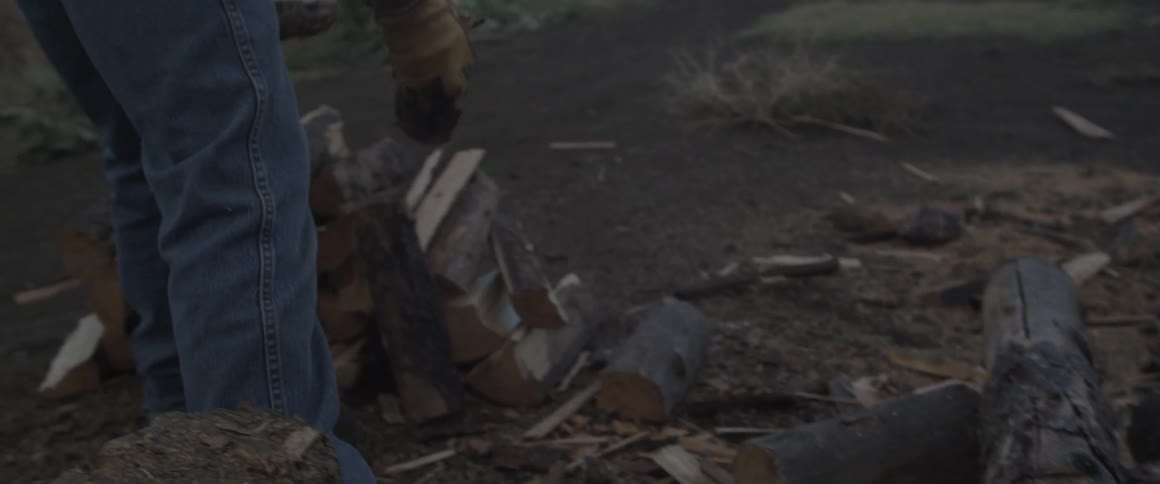 A man picks up cut cords of wood and puts them on a pile