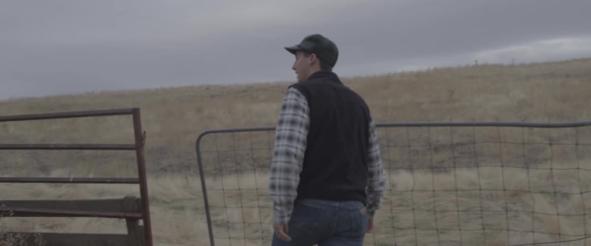 A man walks through an open gate in a field