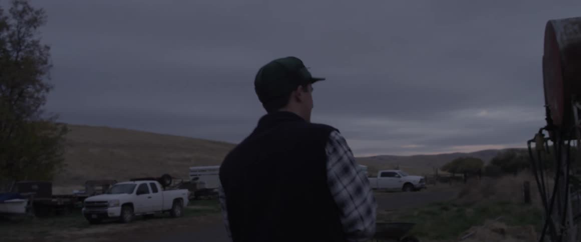 A man walks out in an open field near trucks