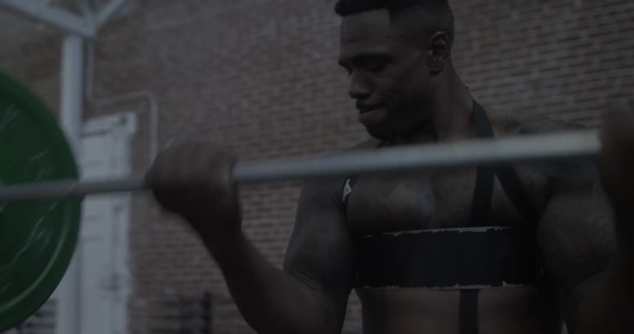 A shirtless man lifts weights in front of a brick wall