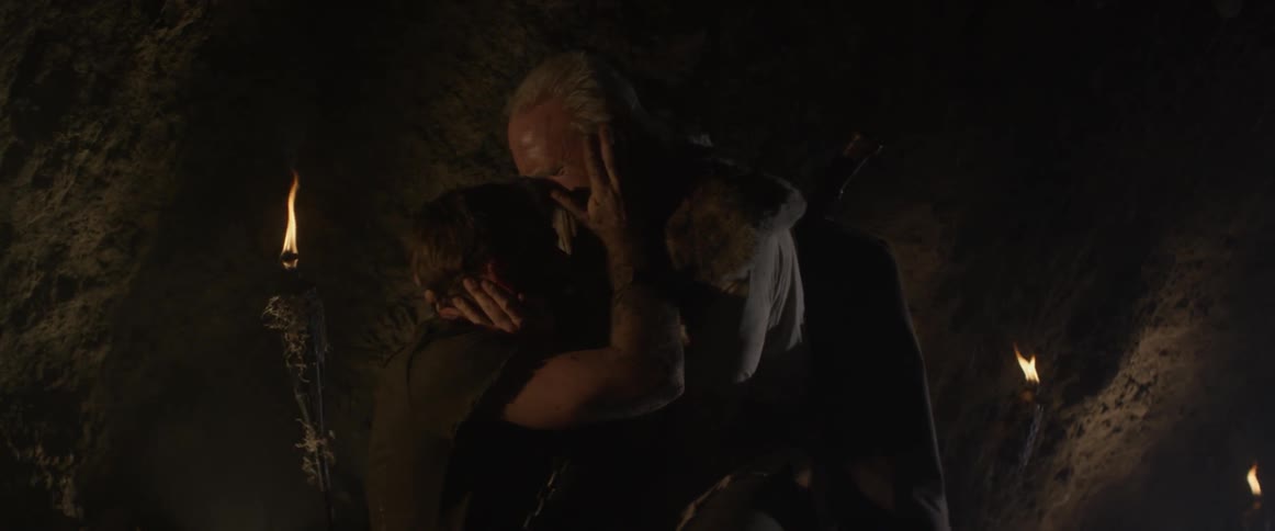A man leans over and holds another man's face