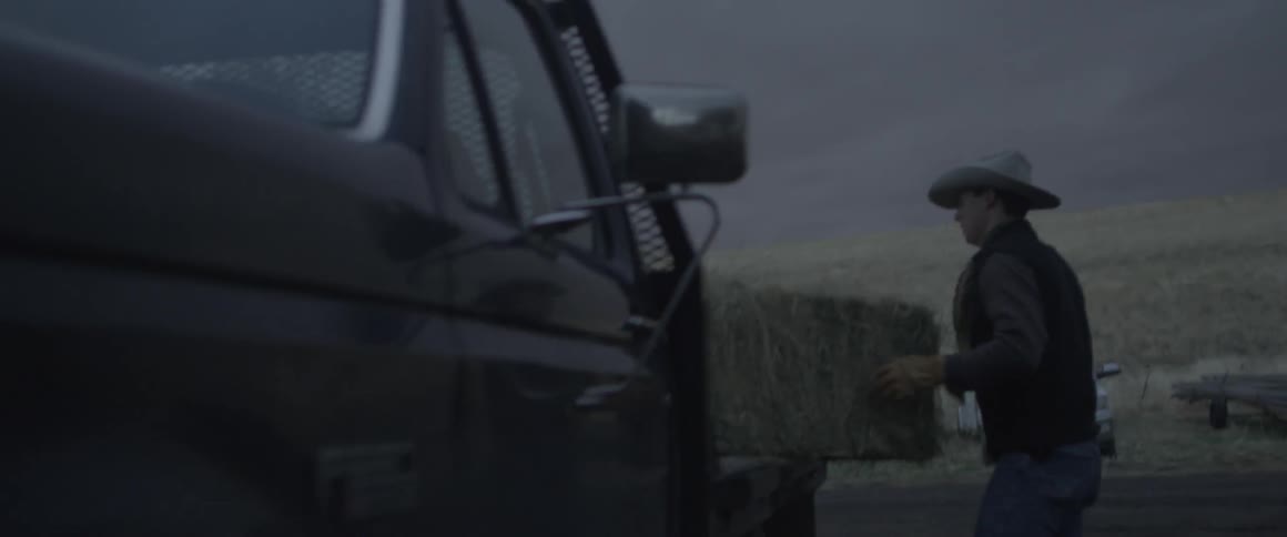 A cowboy loads a bale of hay into the back of a pickup truck