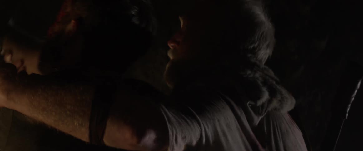 An elderly man tends to a hurt young man in a cave