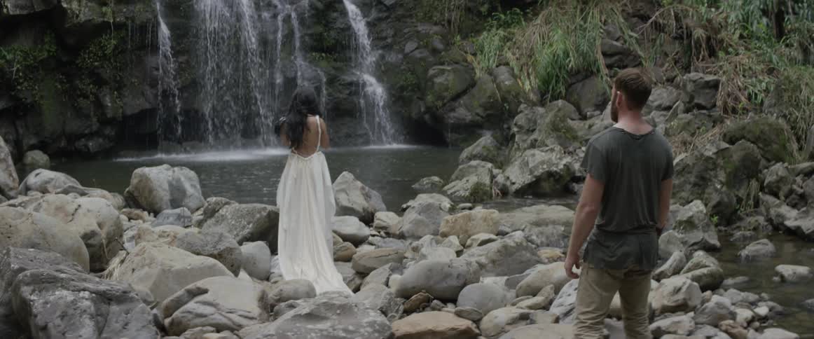 A man walks up to a woman watching a waterfall