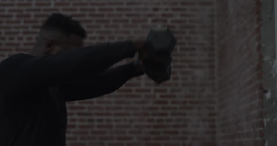 Man lifting dumbbell weight up and down in front of brick wall