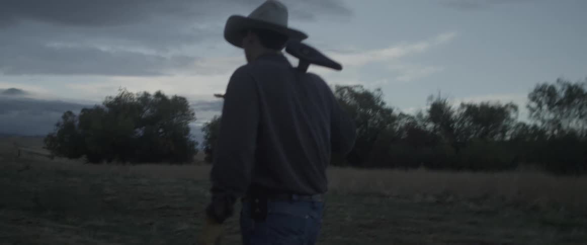 Man in a cowboy hat carries an ax over his shoulder