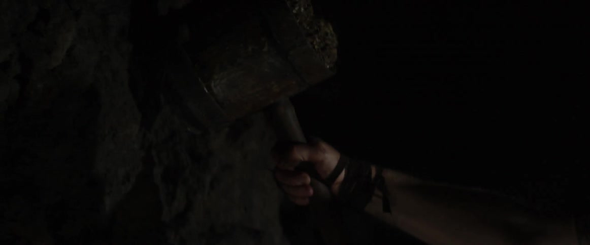 A bearded man swings a hammer at a dirt wall