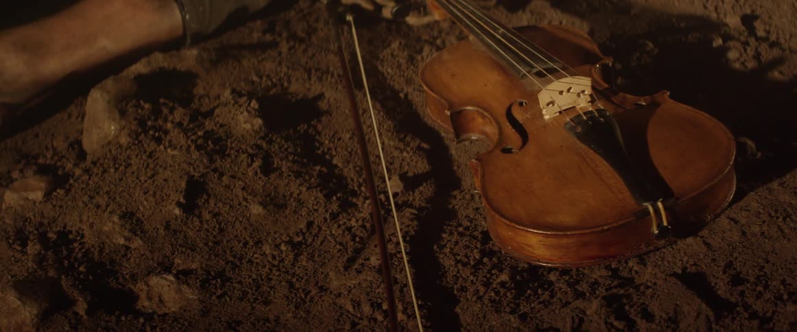 A violin sits on the dirt ground