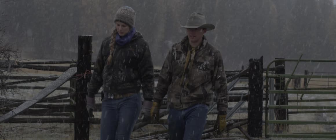 A couple walk on a ranch as snow falls