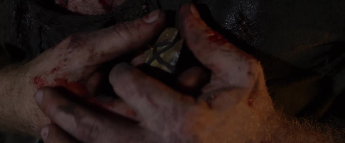 A bleeding man grips a pendant on a necklace