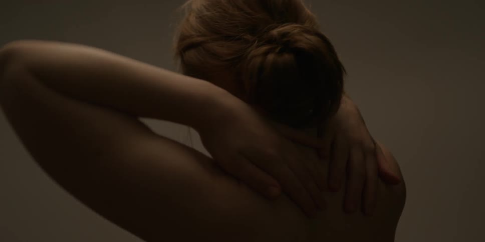 A naked woman rubs her arms on her shoulders and upper back
