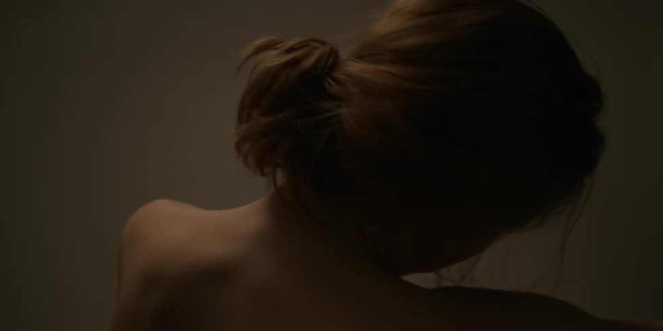 A shirtless woman rubs her hands on her shoulders and stretches her arms outward