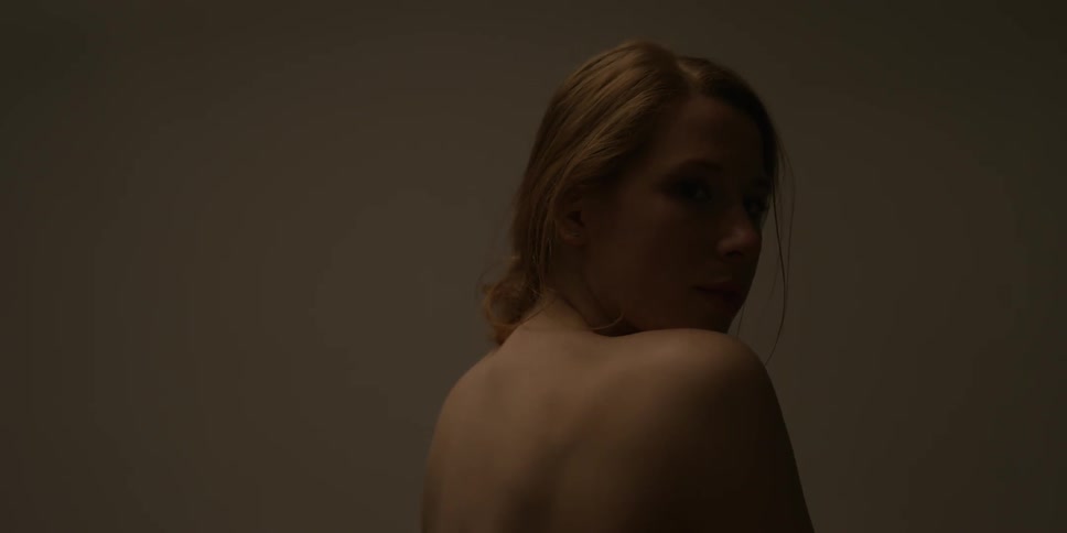 A topless woman looks over her bare shoulder