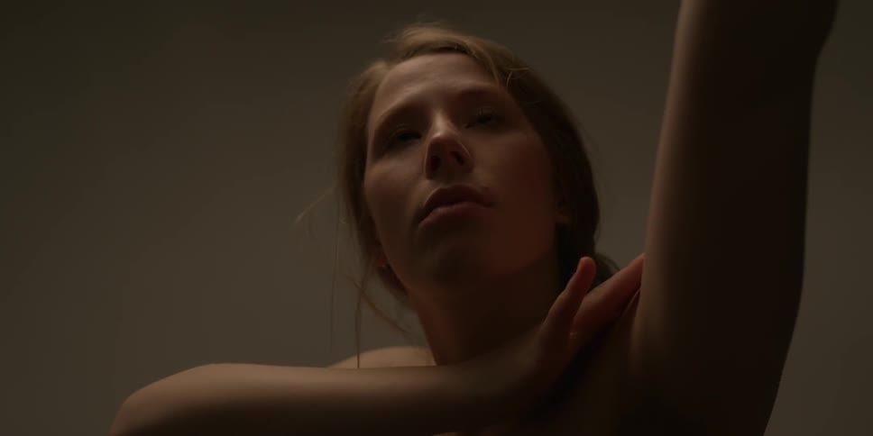 A naked woman caresses her arm as she moves it behind her head