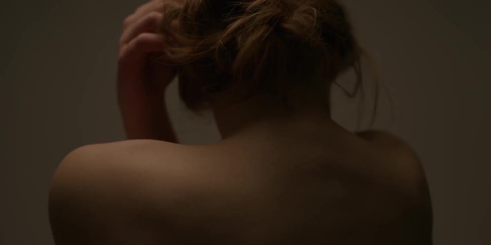 A shirtless woman rolls her head and wraps her arms around her back