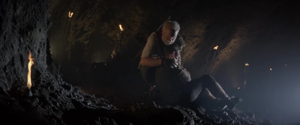 An elderly man consoles a young man in a cave