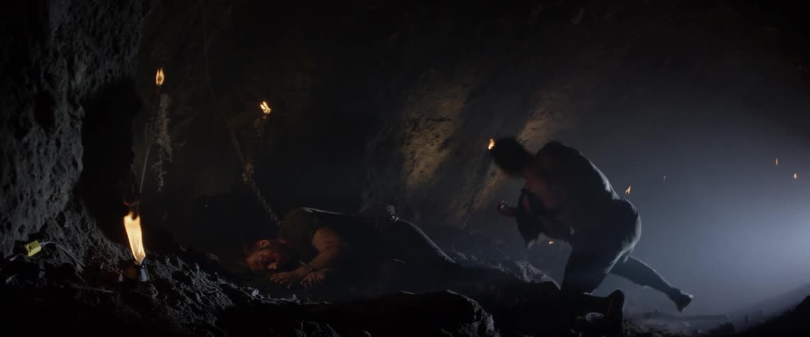 The cave is dark with a man sleeping and torches all over