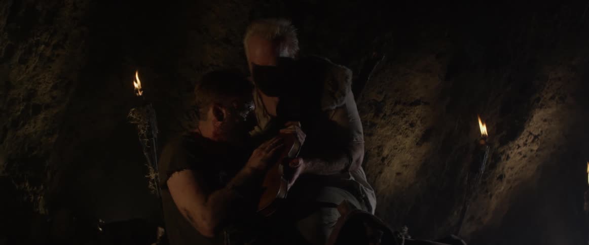 An elderly man pulls a violin out of a bag and gives it to a hurt young man