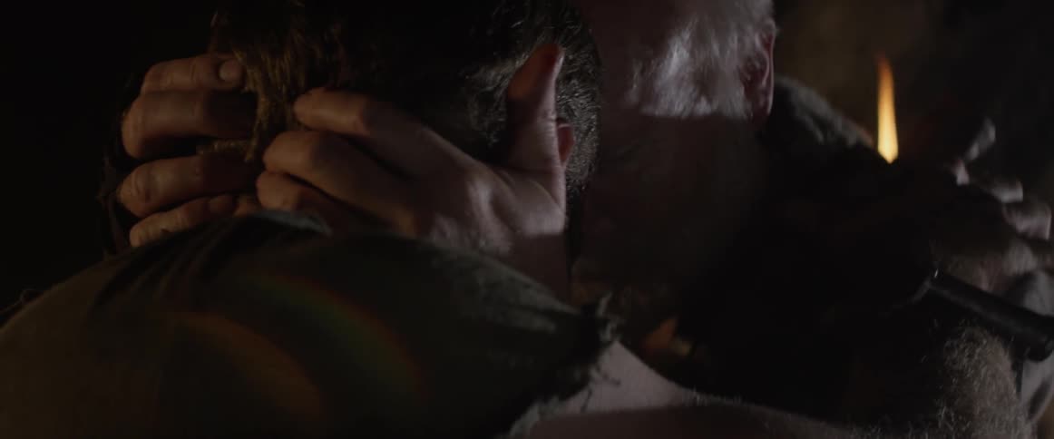 An elderly man consoles a young man in a cave