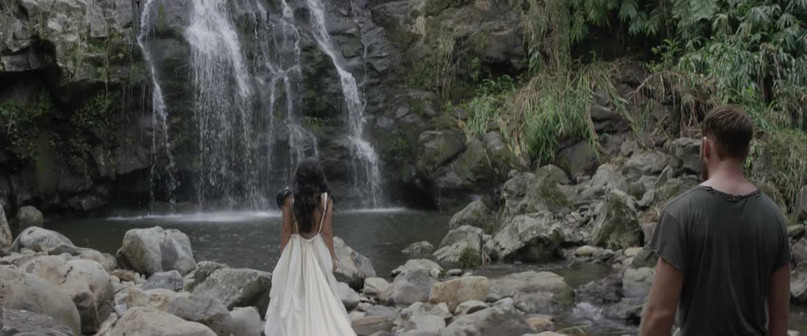A man follows a woman as she walks toward a waterfall