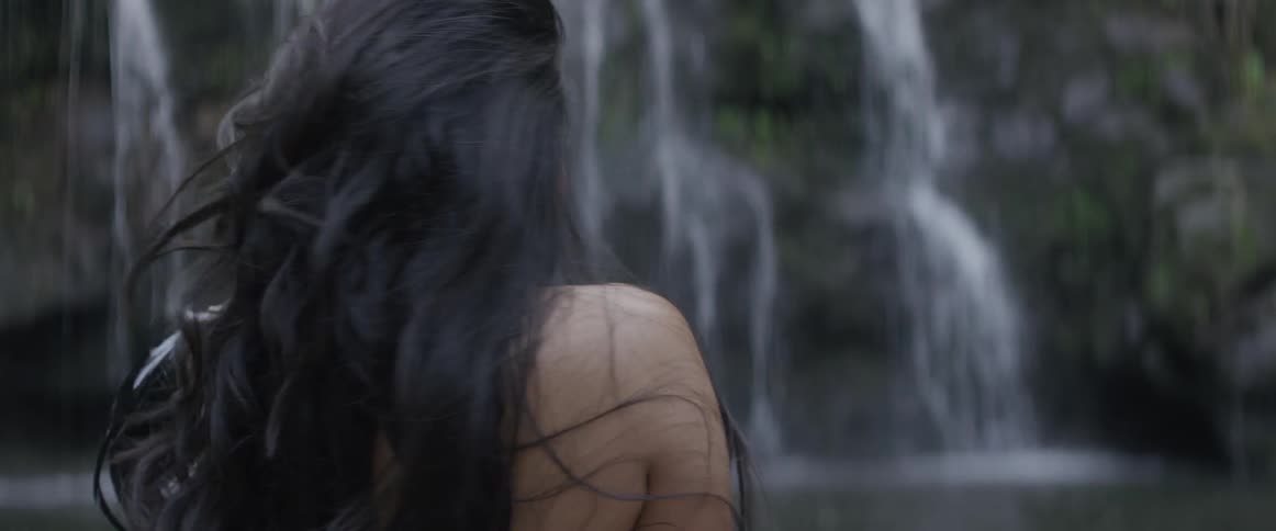 Woman standing in front of a waterfall looks back over her shoulder