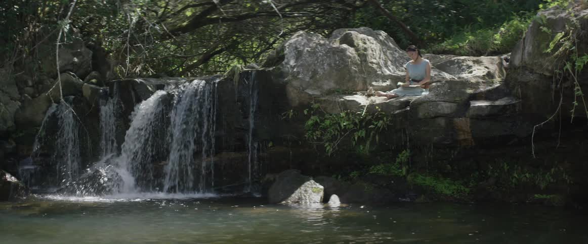 Woman sits on rocks near a waterfall