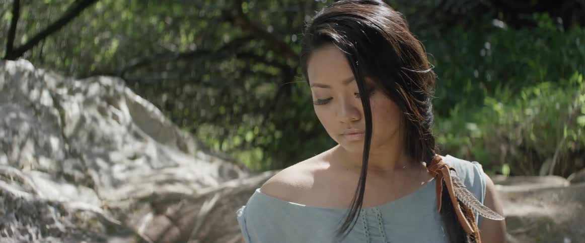Woman stands outside near rocks and trees on a sunny day