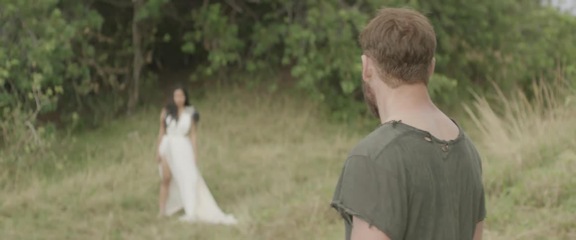 A man is following a woman in a white dress into the forest