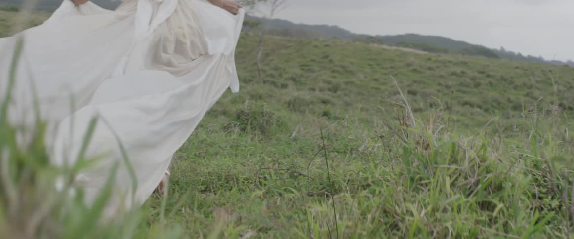 A woman wearing a white dress runs through a field