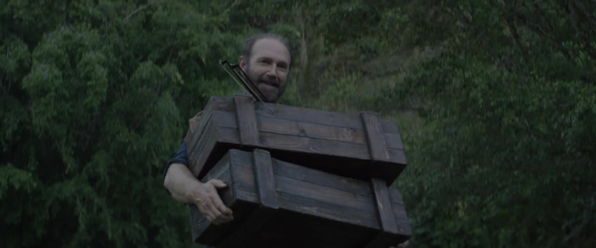 A man smiles as he carries two wooden boxes