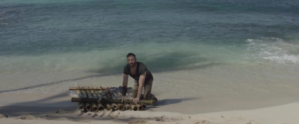 A man kneels on a raft by the water on the beach