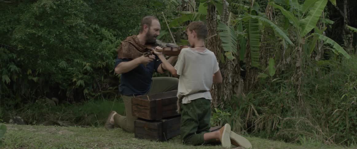 A man and boy play violins together by the forest