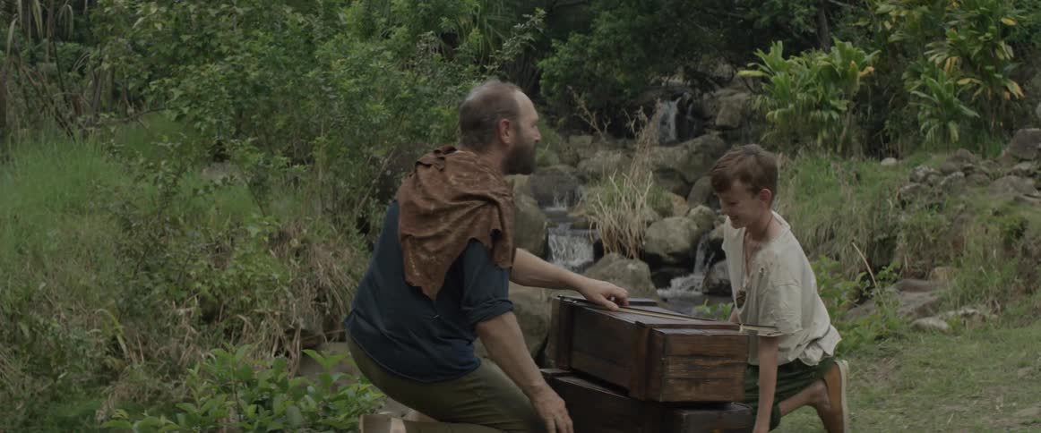 Man and boy kneeling by wooden boxes near a stream