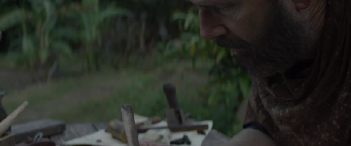 An older man is using a knife to carve something into a piece of wood